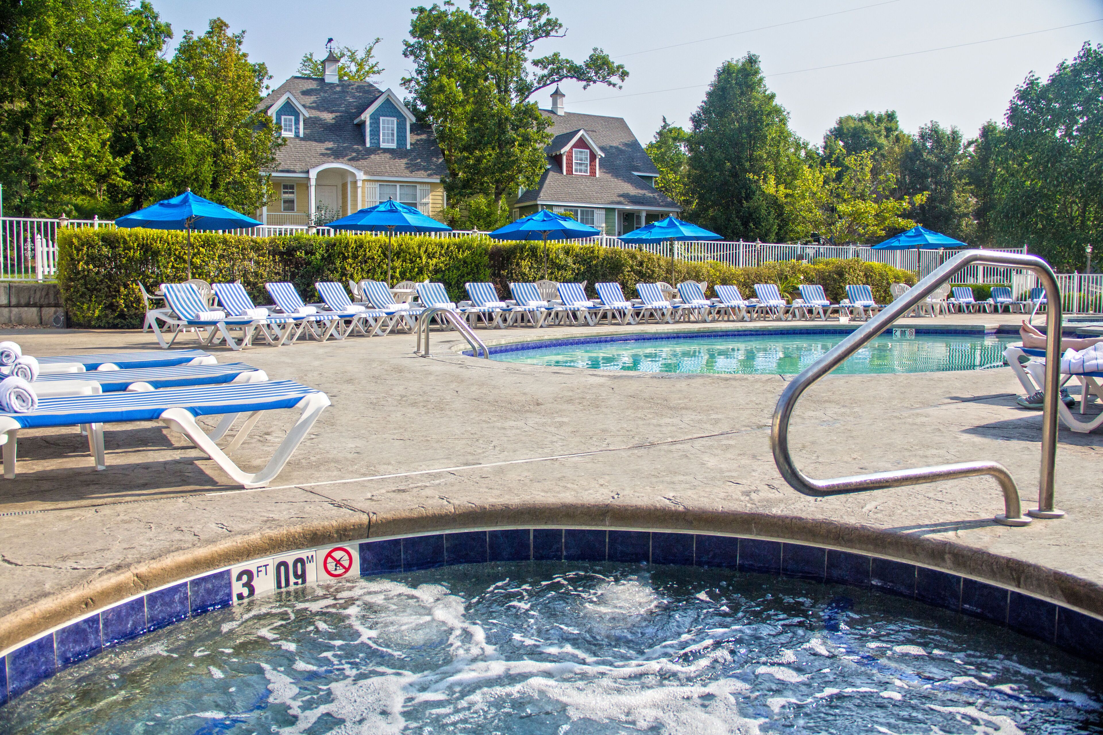 Un espace piscine comprenant des chaises longues et des parasols, un jacuzzi et une clôture entourant la piscine.