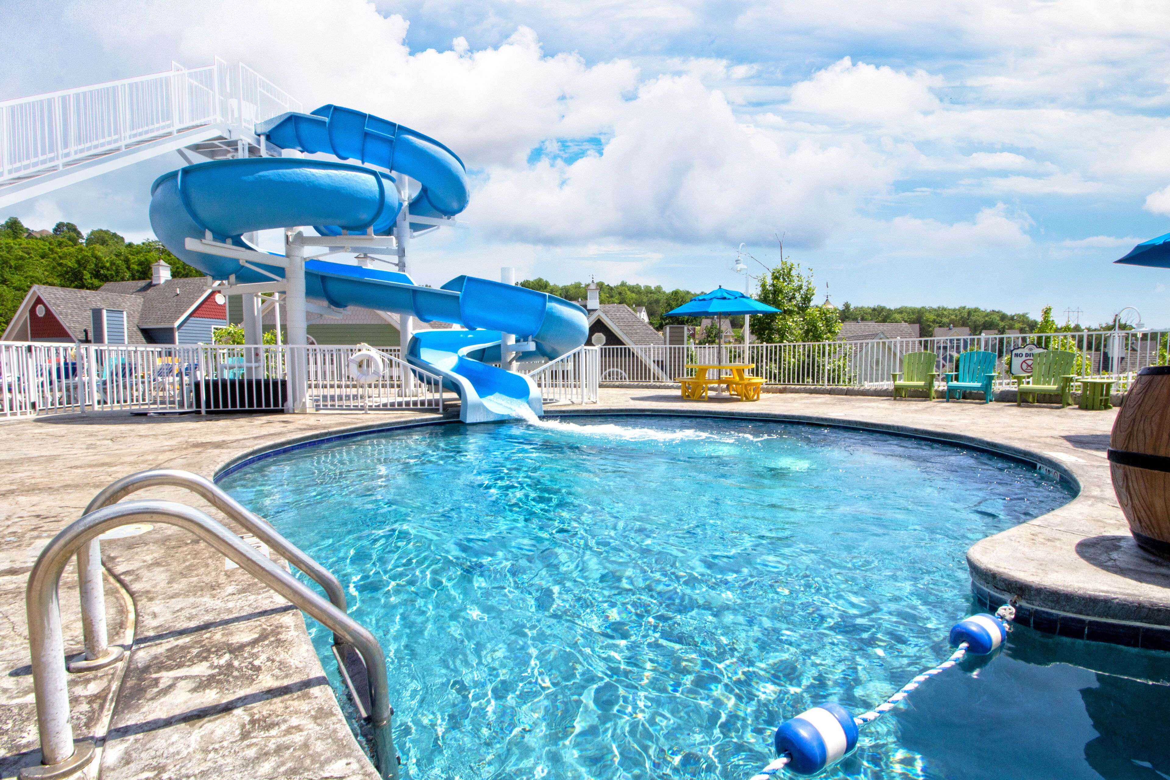 A swimming pool with a water slide, a metal ladder, and a fence.