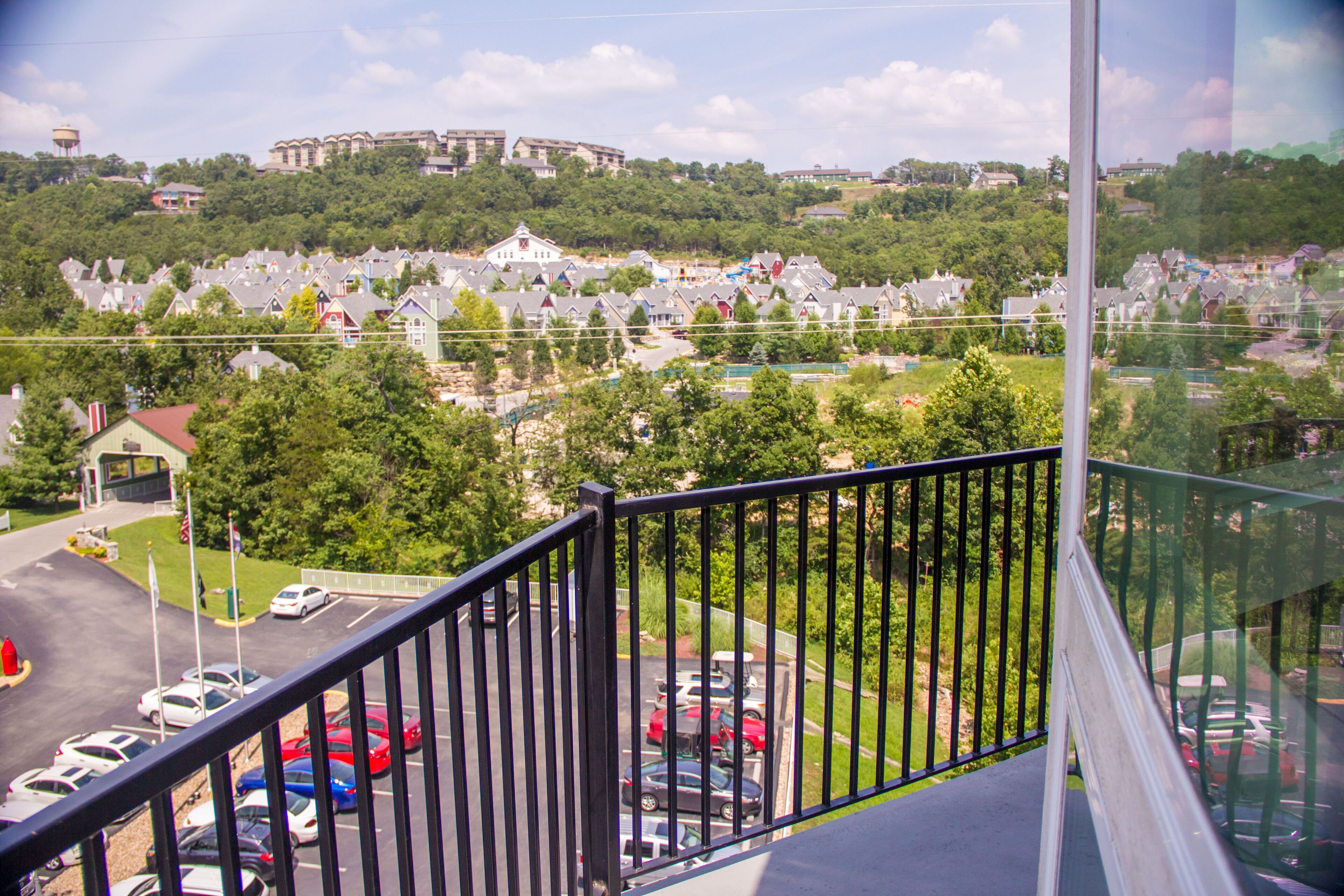 Une vue depuis un balcon donnant sur un parking et une zone résidentielle avec des maisons et de la verdure.