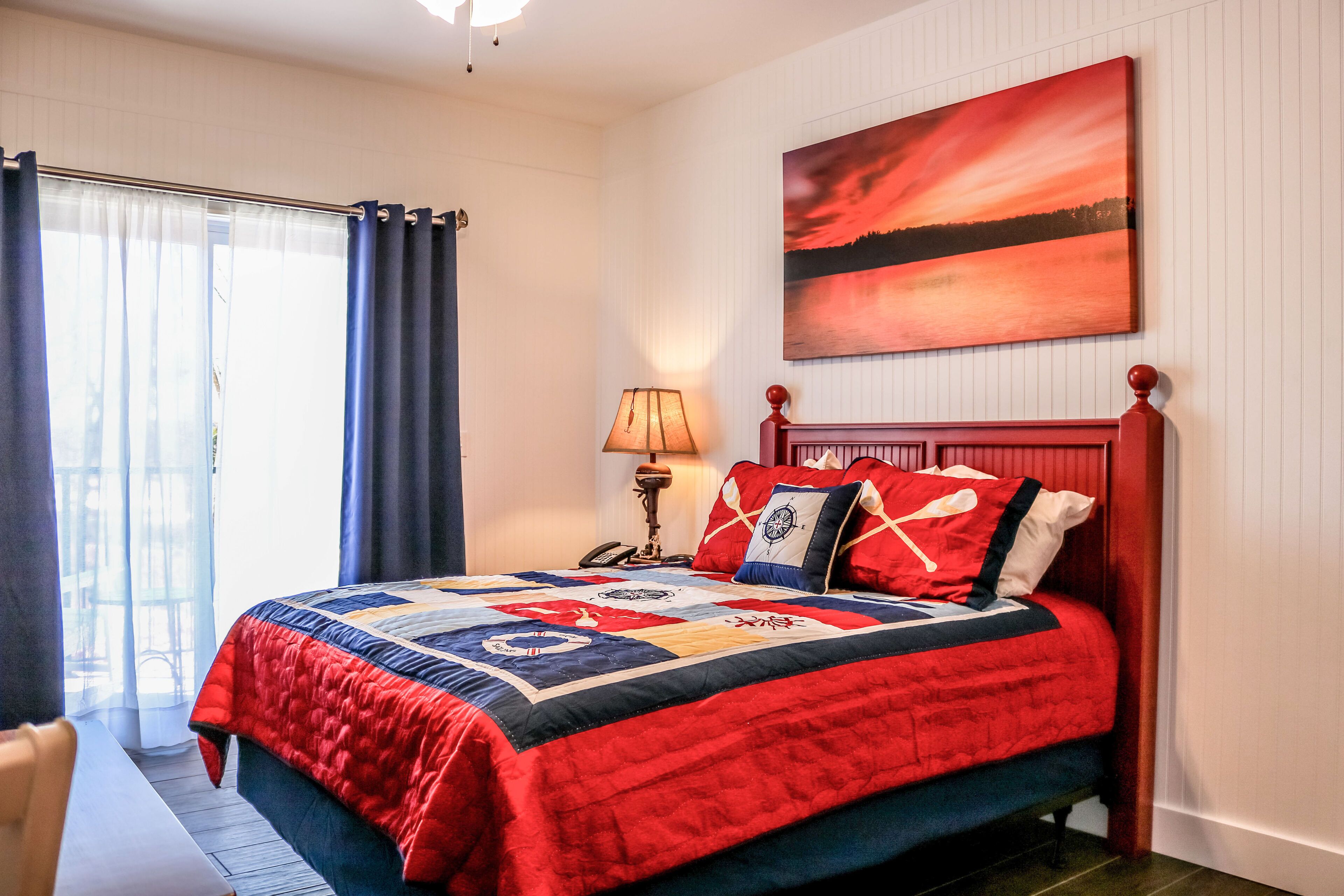 A bedroom with a large bed, a nightstand, a lamp, and a painting on the wall.