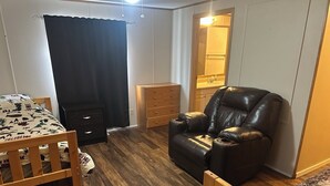 Una habitación con una cama de madera, un sillón de cuero negro, un aparador de madera y un espejo.