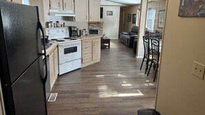 Una cocina compacta con refrigerador, estufa y alacenas. Hay un comedor con sillas y una mesa.