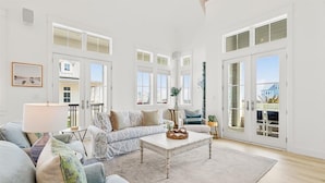A spacious living room with a large sofa, a coffee table, and a view through the glass doors. - Red White and Saguaro 246 DEW (Port Aransas)