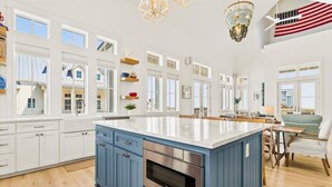 A spacious kitchen with a large island, white cabinetry, and a blue accent wall. - Red White and Saguaro 246 DEW (Port Aransas)