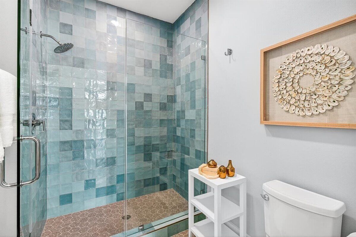 A modern bathroom with a glass shower enclosure, a white toilet, and a small white shelf with decorative items.
