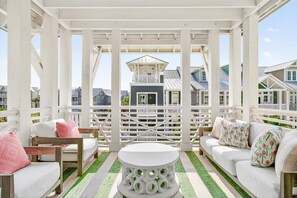 A covered outdoor seating area with white furniture, a central white table, and a view of houses in the background. - Shangri-lala TC 6305 (Port Aransas)