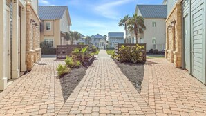 A paved walkway leading to a row of two-story houses with a clear sky above. - Dnas Dunes TC 2202 (Port Aransas)