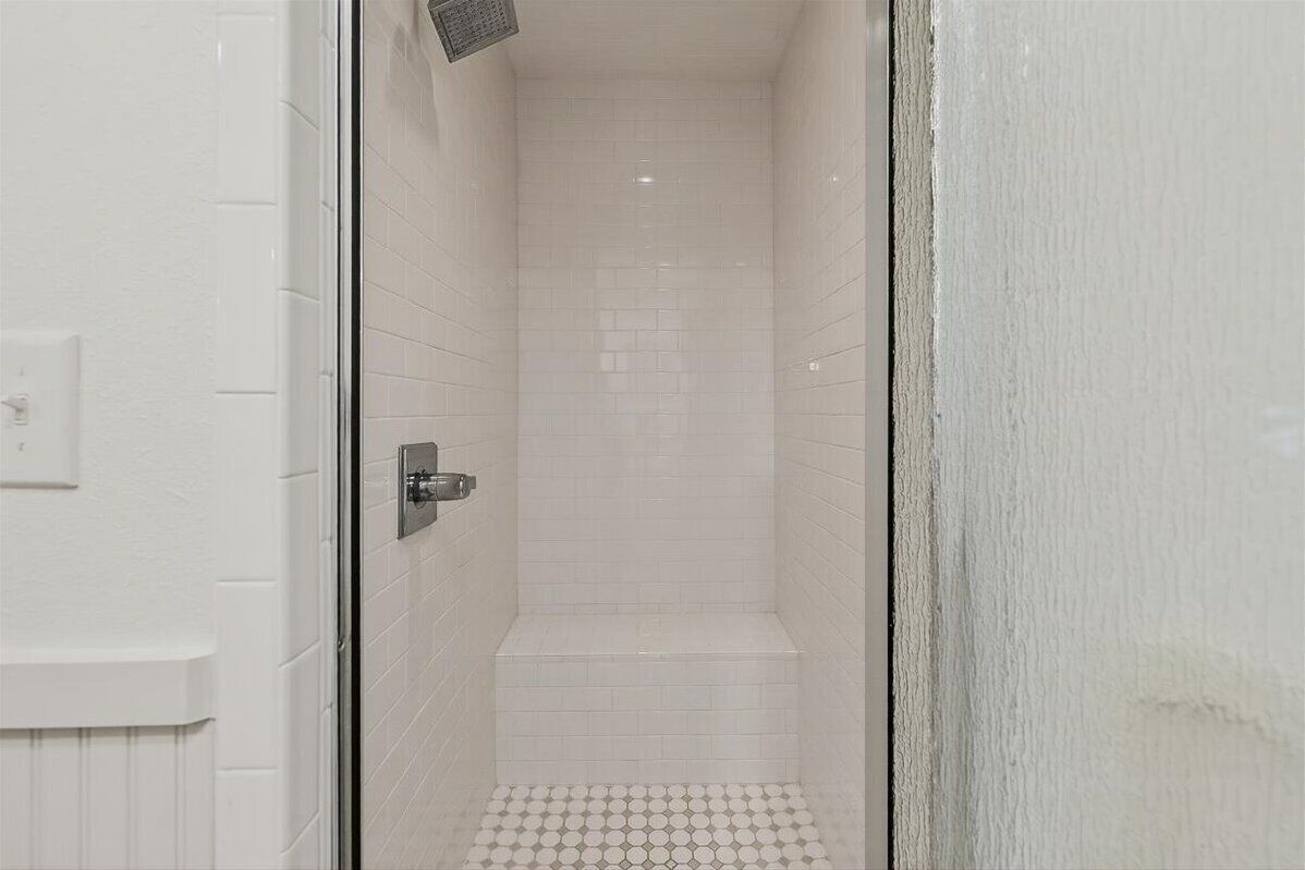 A narrow, tiled shower area with a white door and a visible shower control panel.