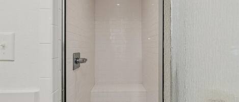 A narrow, tiled shower area with a white door and a visible shower control panel.