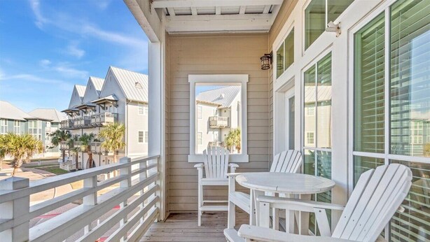 A wooden deck with white chairs and a table, overlooking a residential area with similar houses. - Dnas Dunes TC 2202 (Port Aransas)