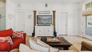 A living room with a white wall, a red sofa, a wooden coffee table, and a TV on a white cabinet. - Dnas Dunes TC 2202 (Port Aransas)