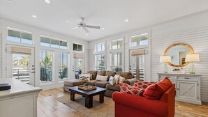 A spacious living room with a large window, a ceiling fan, a red sofa, and a wooden coffee table. - Dnas Dunes TC 2202 (Port Aransas)