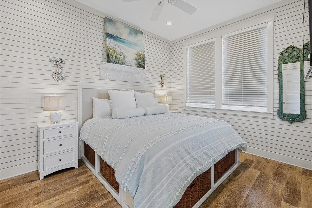 A bedroom with a bed, nightstands, a mirror, and a window with blinds.