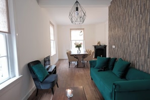A living room with a green sofa, a dining table with chairs, a fireplace, and a window with a view.