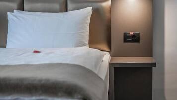 Ein modernes Hotelzimmer mit einem gepolsterten Kopfteil, einer Nachttischlampe und einem Bedienfeld auf dem Nachttisch.