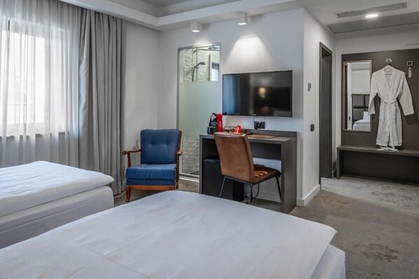 A hotel room with two beds, a desk, a chair, a TV, a robe, and a shower area. - CHARM BOUTIQUE HOTEL (Satu Mare)