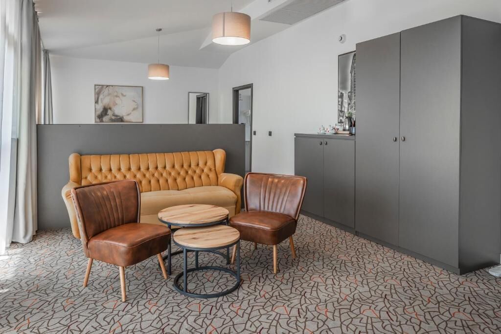A modern room with a tufted sofa, leather chairs, a small round table, and a grey wardrobe.