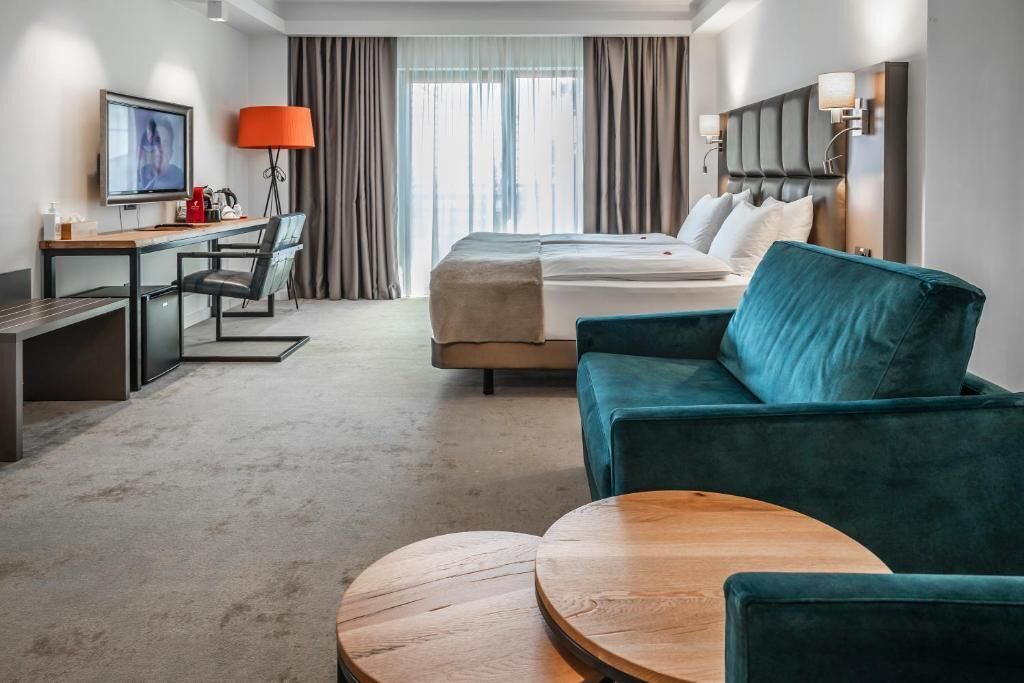 Habitación de hotel con cama, escritorio, silla, televisión, lámpara y una mesa de centro redonda.