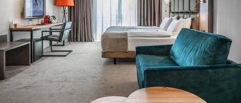 Habitación de hotel con cama, escritorio, silla, televisión, lámpara y una mesa de centro redonda.