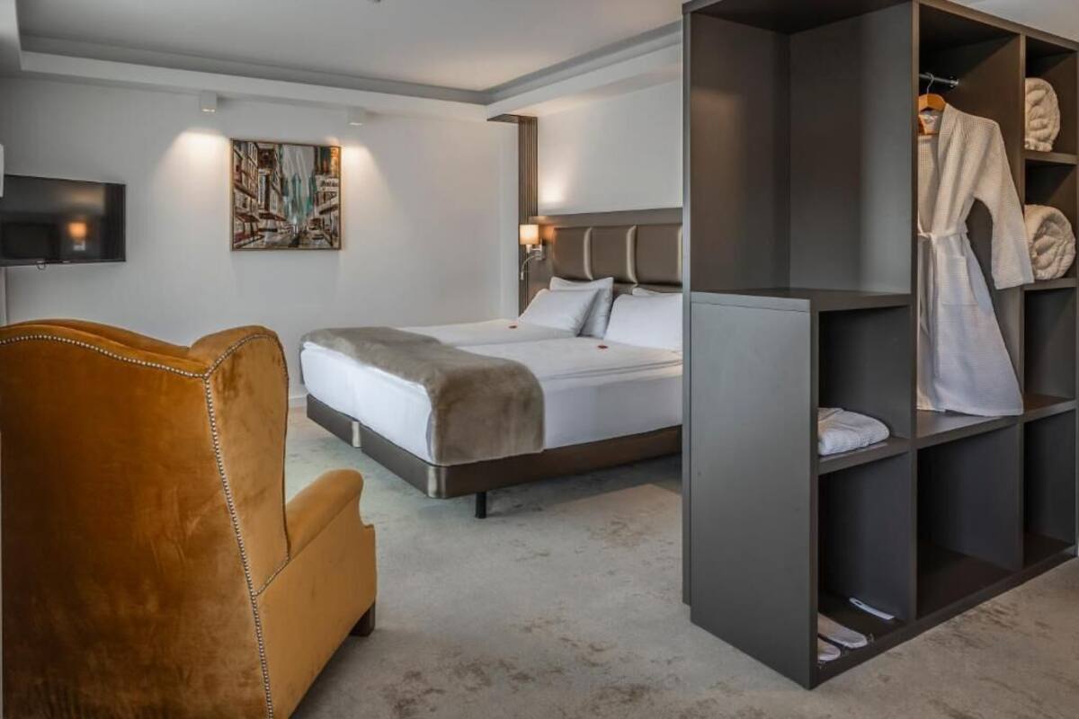 Moderni hotellihuone, jossa on suuri sänky, oleskelualue, vaatekaappi ja seinälle asennettu taulutelevisio.