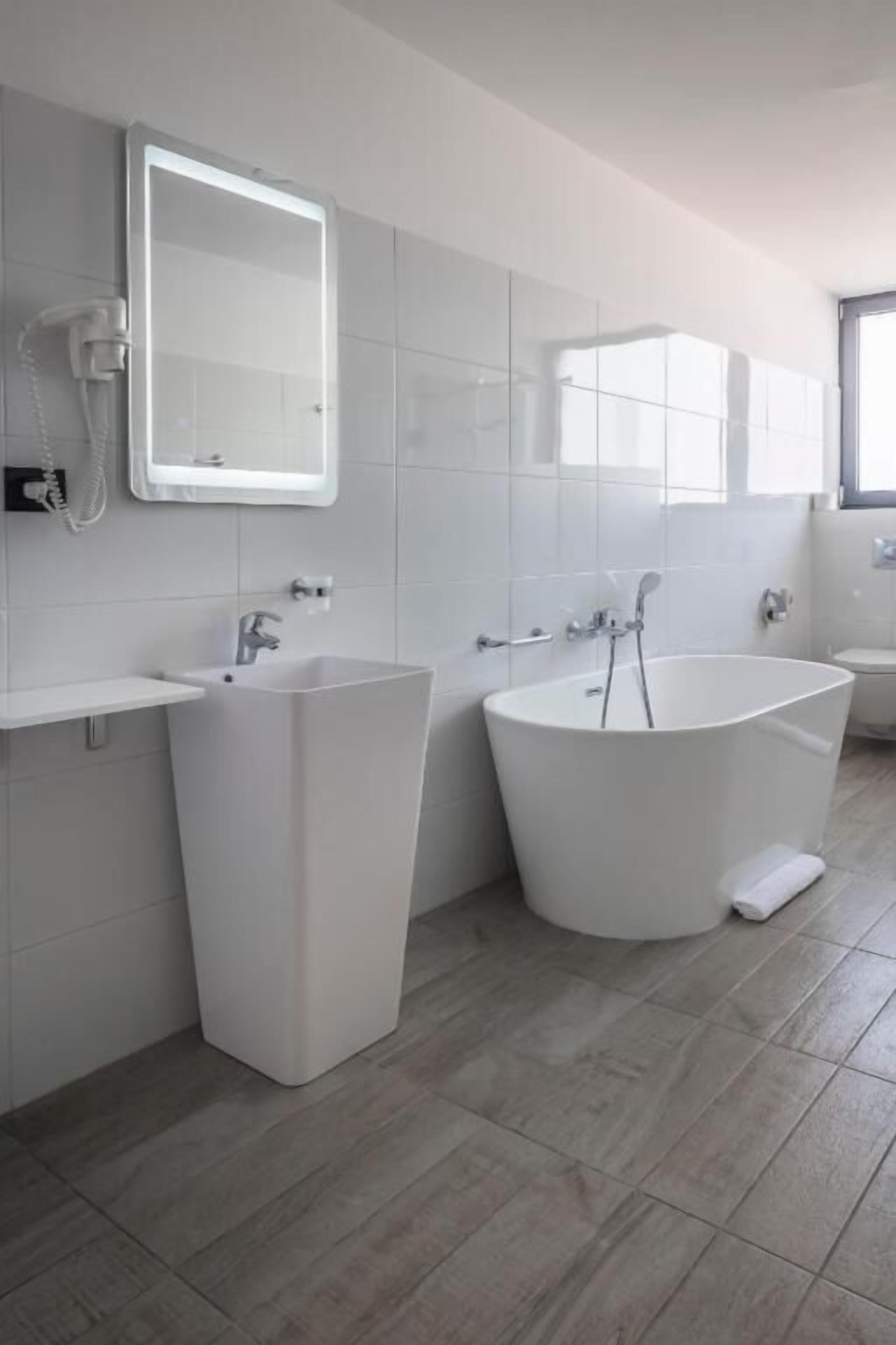 Une salle de bain moderne avec une grande baignoire, un lavabo sur colonne et un miroir au-dessus du lavabo.