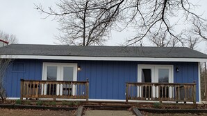 Una casa a un piano con facciata blu, due finestre frontali e un portico in legno con ringhiere.
