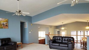 Un salon avec un canapé en cuir noir, un banc en bois et un ventilateur de plafond.