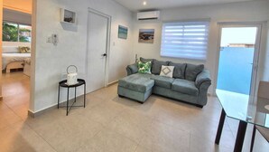 Una sala moderna con un sofá gris, una mesa de centro de vidrio y una mesita auxiliar.