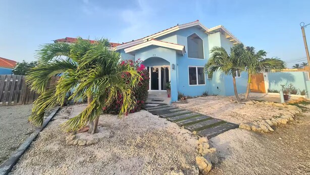 Una casa de dos pisos con fachada azul claro, una terraza de madera y un camino de entrada de grava.