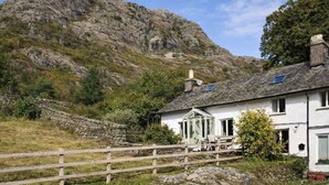 A white house with a stone wall, a wooden fence, and a mountain in the background. - Poppy Cottage - Coniston - Pass the Keys (Coniston)