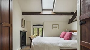 A bedroom with a bed, wooden beams, a skylight, a fireplace, and a door. - Poppy Cottage - Coniston - Pass the Keys (Coniston)