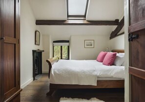 Ein Schlafzimmer mit einem Bett, Holzbalken, einem Oberlicht, einem Kamin und einer Tür.