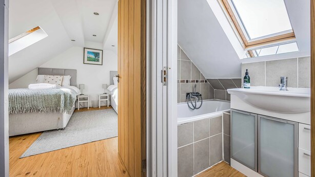 Ein modernes Schlafzimmer mit Oberlicht, einem eigenen Badezimmer mit Badewanne und einem kleinen Nachttisch.
