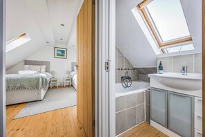 A modern bedroom with a skylight, a separate bathroom with a bathtub, and a small bedside table. - Gorgeous Bosham Family Home w Garden - Pass the Keys (Chichester)