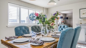 Ein Essbereich mit einem Holztisch, gedecktem für sechs Personen, blauen Polsterstühlen und einer Vase mit Blumen.