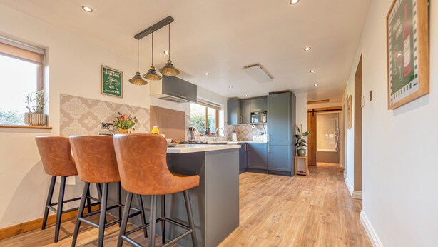 A modern kitchen with a central island, bar stools, pendant lighting, and a view to the dining area. - Spacious 4-Bed in Peaceful Market Drayton - Pass the Keys (Lockleywood)