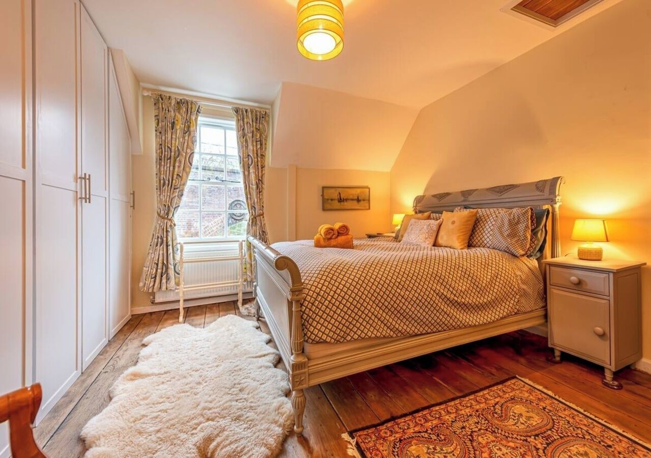 Un dormitorio con cama, mesita de noche y ventana con cortinas.
