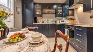Una cocina moderna con armarios oscuros, una mesa de comedor con mantel de encaje y una fuente de fruta.
