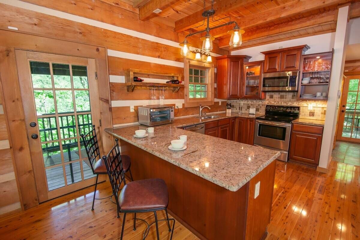 A wooden cabin interior with a kitchen featuring granite countertops, wooden cabinets, and a bar area with stools.