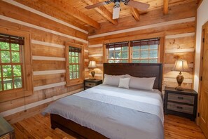 Ein Schlafzimmer in einer Blockhütte mit einem großen Bett, zwei Nachttischen mit Lampen und einem Deckenventilator.