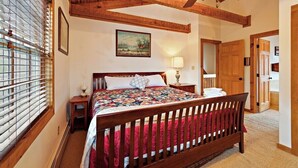 Een slaapkamer met een houten bed, een schilderij aan de muur en een raam met jaloezieën.