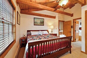 A bedroom with a wooden bed, a painting on the wall, and a window with blinds. - Game Room, Hot Tub, Fire Pit, Close to Skiing (Seven Devils)