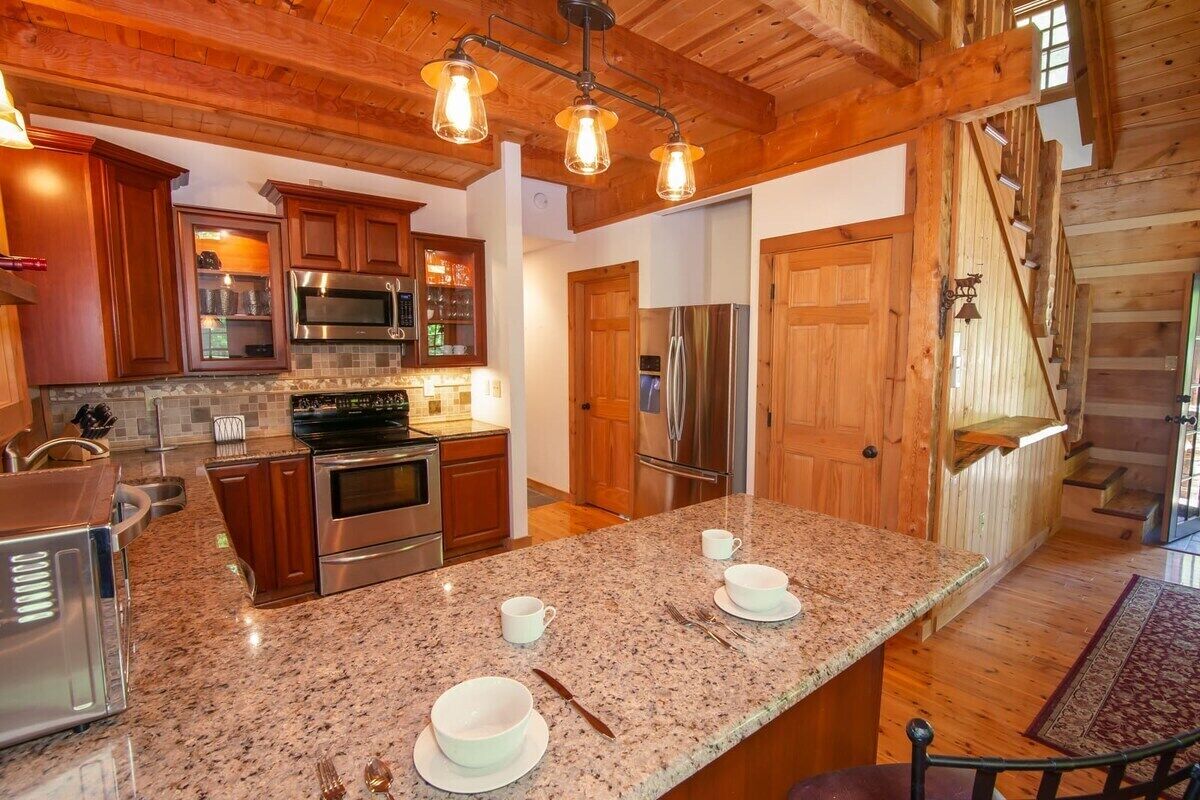 A kitchen with granite countertops, stainless steel appliances, wooden cabinets, and a central island with seating.
