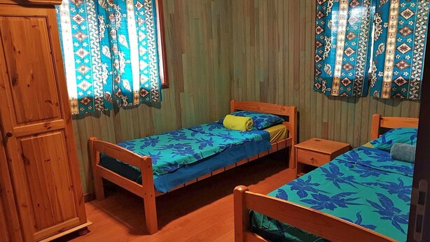 Una habitación pequeña y acogedora con dos camas de madera, un armario de madera y cortinas con estampado.