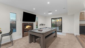 Un salon moderne avec une table de billard, une cheminée et un grand téléviseur fixé au mur.