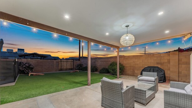 Une terrasse extérieure aménagée avec des meubles en osier, un barbecue et une fresque représentant un coucher de soleil sur le mur.
