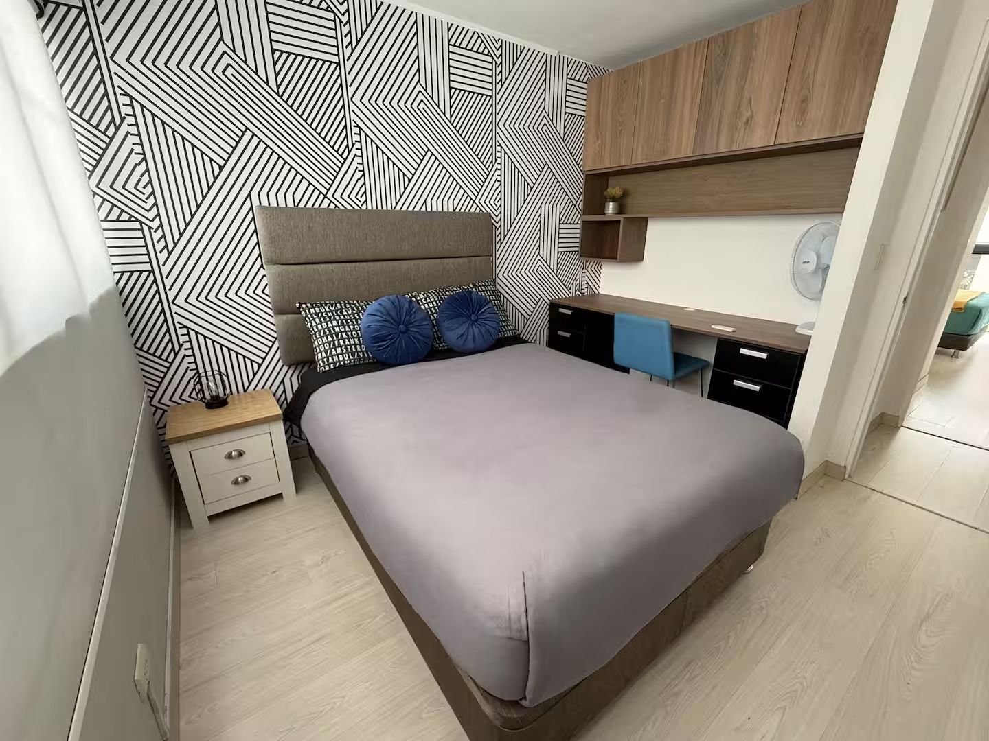 A modern bedroom with a bed, bedside tables, a desk, and a patterned wall.