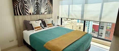 A modern bedroom with a large bed, a zebra-patterned artwork above the bed, and a city view through a large window.