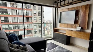 Ein modernes Wohnzimmer mit großem Fenster, einer Couch, einem an einer Holzwand befestigten Fernseher und einem kleinen Tisch.