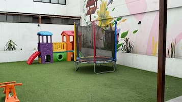 Espaço de recreação infantil com um trampolim e estruturas coloridas sobre grama sintética.